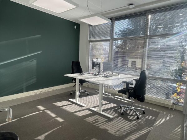 Licht en modern kantoor aan de Jan Leentvaarlaan met twee bureaus, bureaustoelen en grote ramen met jaloezieën.